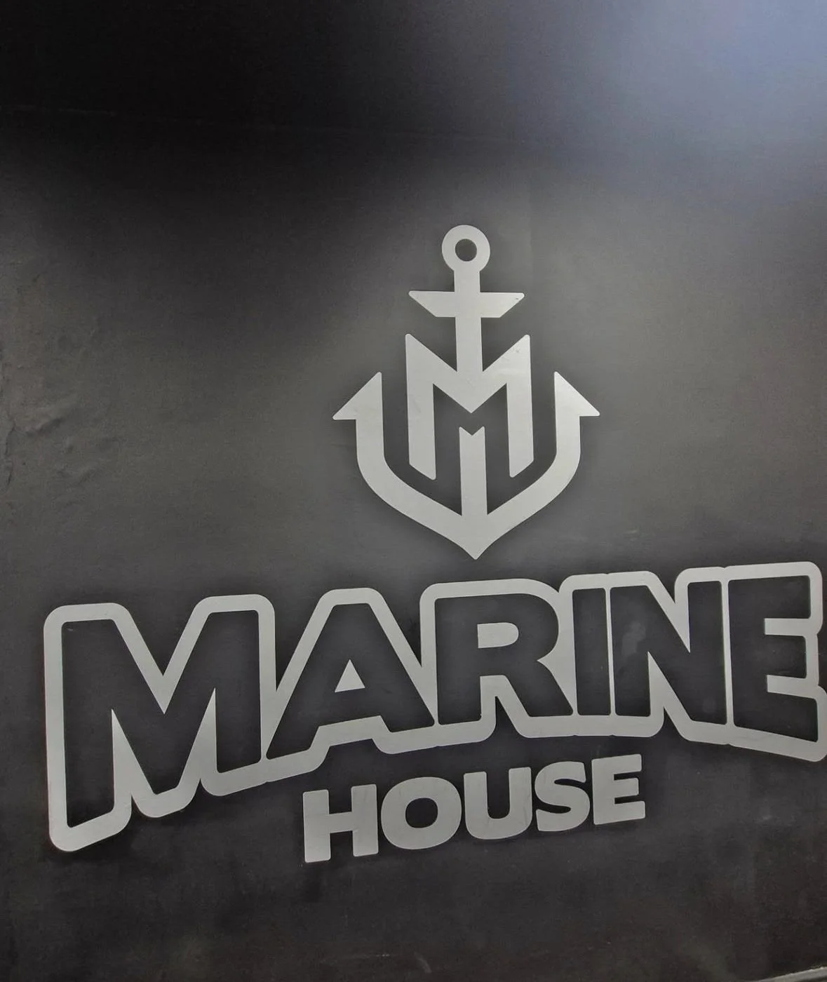 Logo of Marine House with an anchor and a stylized letter M above the text 'MARINE HOUSE' in bold white letters on a dark background.