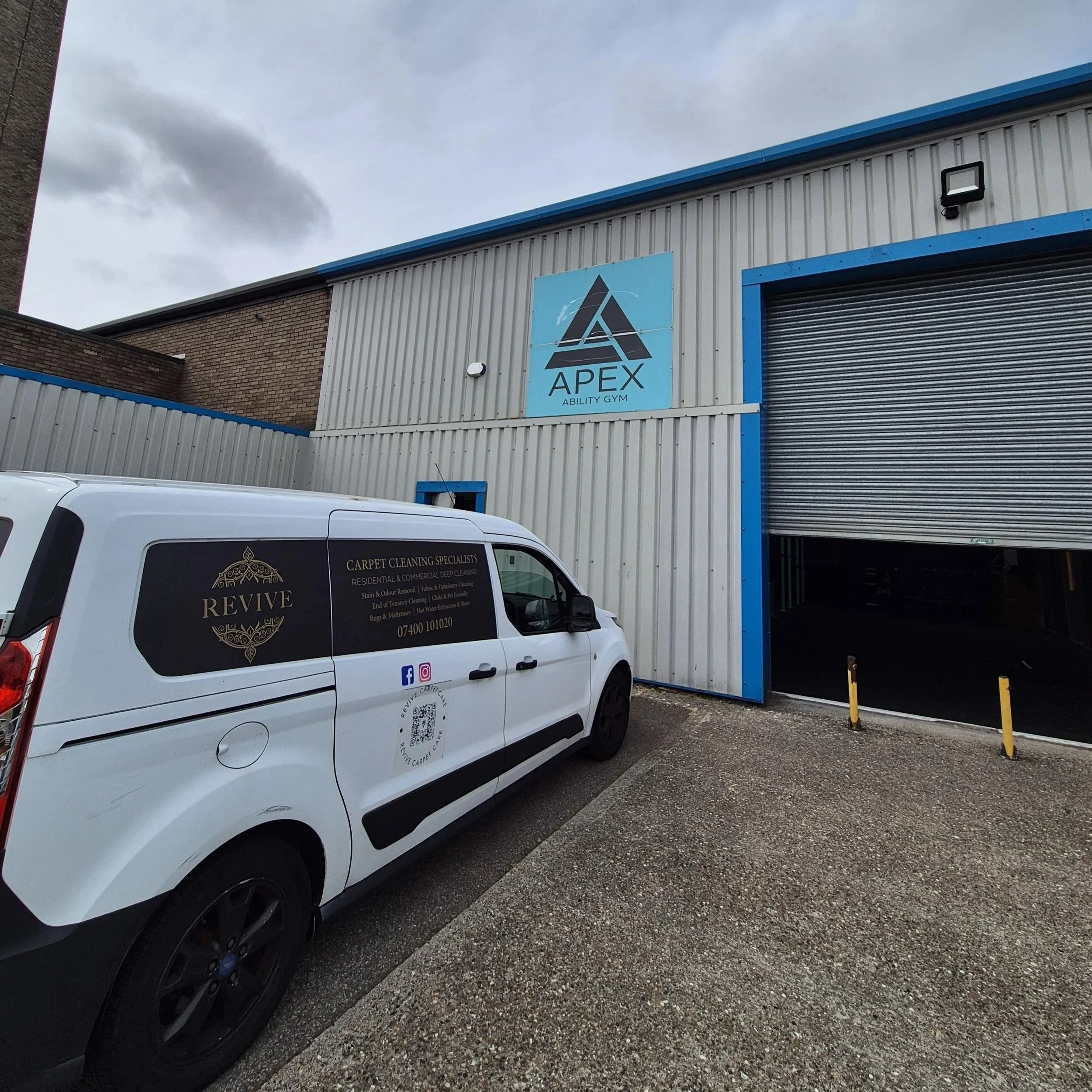 A white van parked in front of a building with a sign that reads 'APEX Ability Gym'. The van has a logo and text advertising carpet cleaning services, including details about the services they offer and their contact information.
