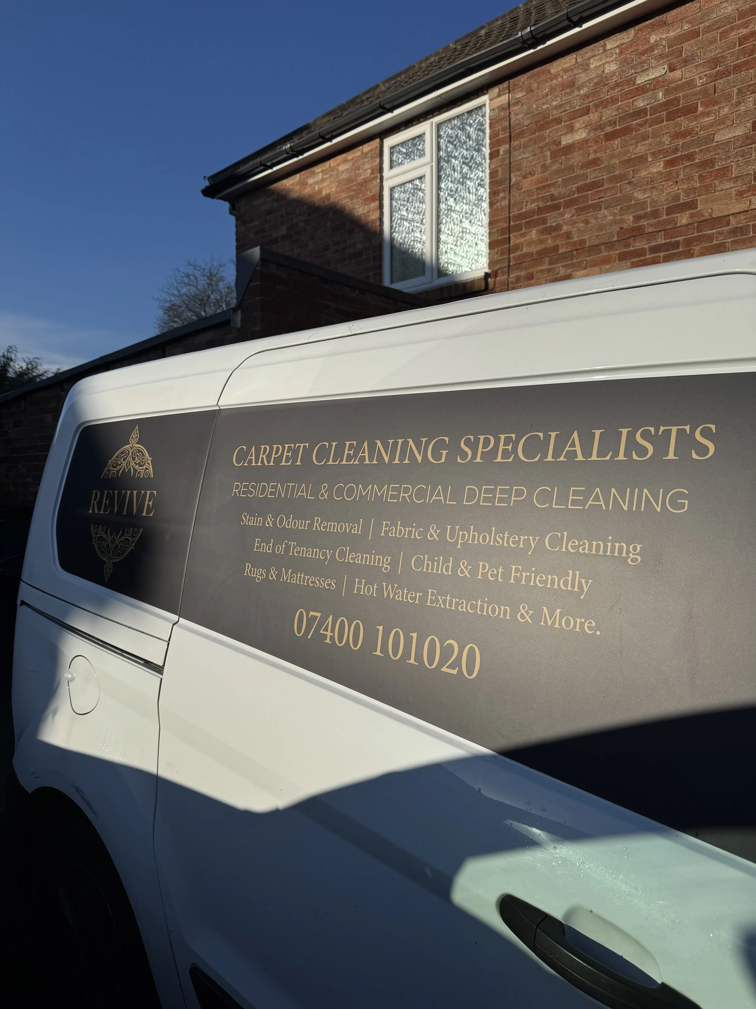 White van with logo and text advertising carpet cleaning services parked in front of a brick house.