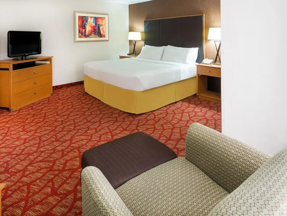 King suite hotel room with a king sized bed, lounge chair, dresser with a TV and nightstands