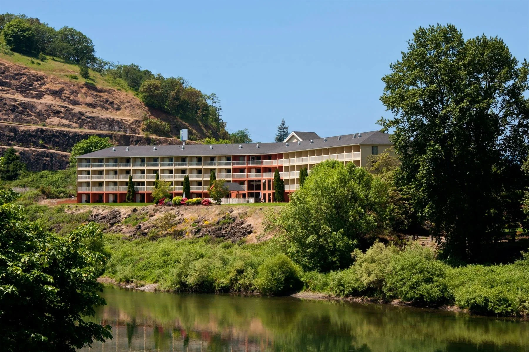 Hotel building with guestroom balconies located alongside a river and lush foliage