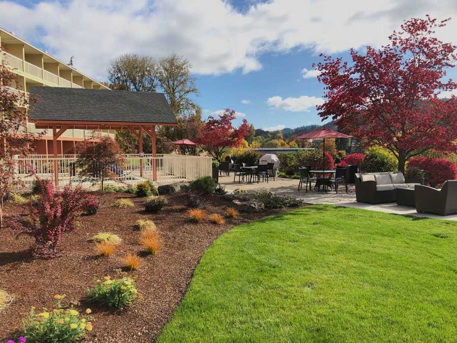 Hotel outdoor patio with tables, chairs and umbrellas upon a grassy lawn with distant green hills