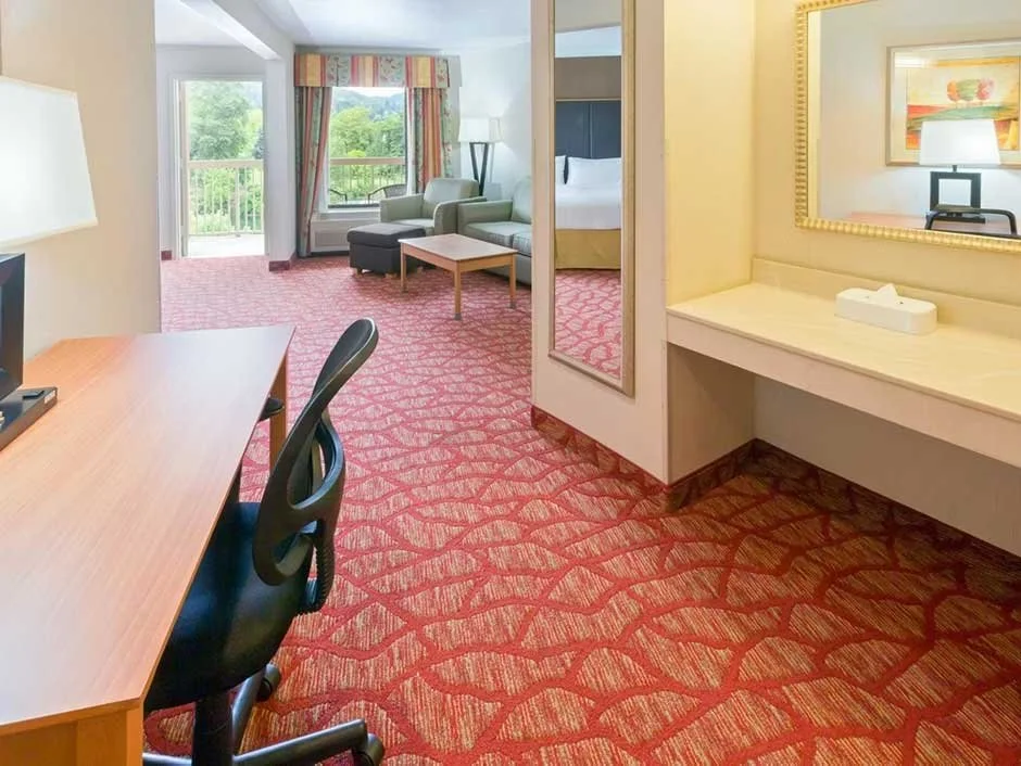 Hotel suite with a desk, vanity mirror and living area with a pull-out sofa overlooking a private balcony 