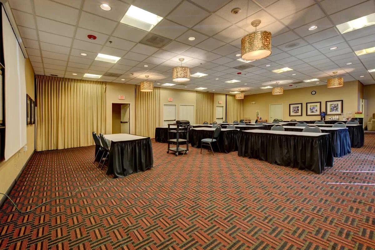 Hotel meeting room with rows of tables and chairs arranged in front of a projector screen for a large conference 