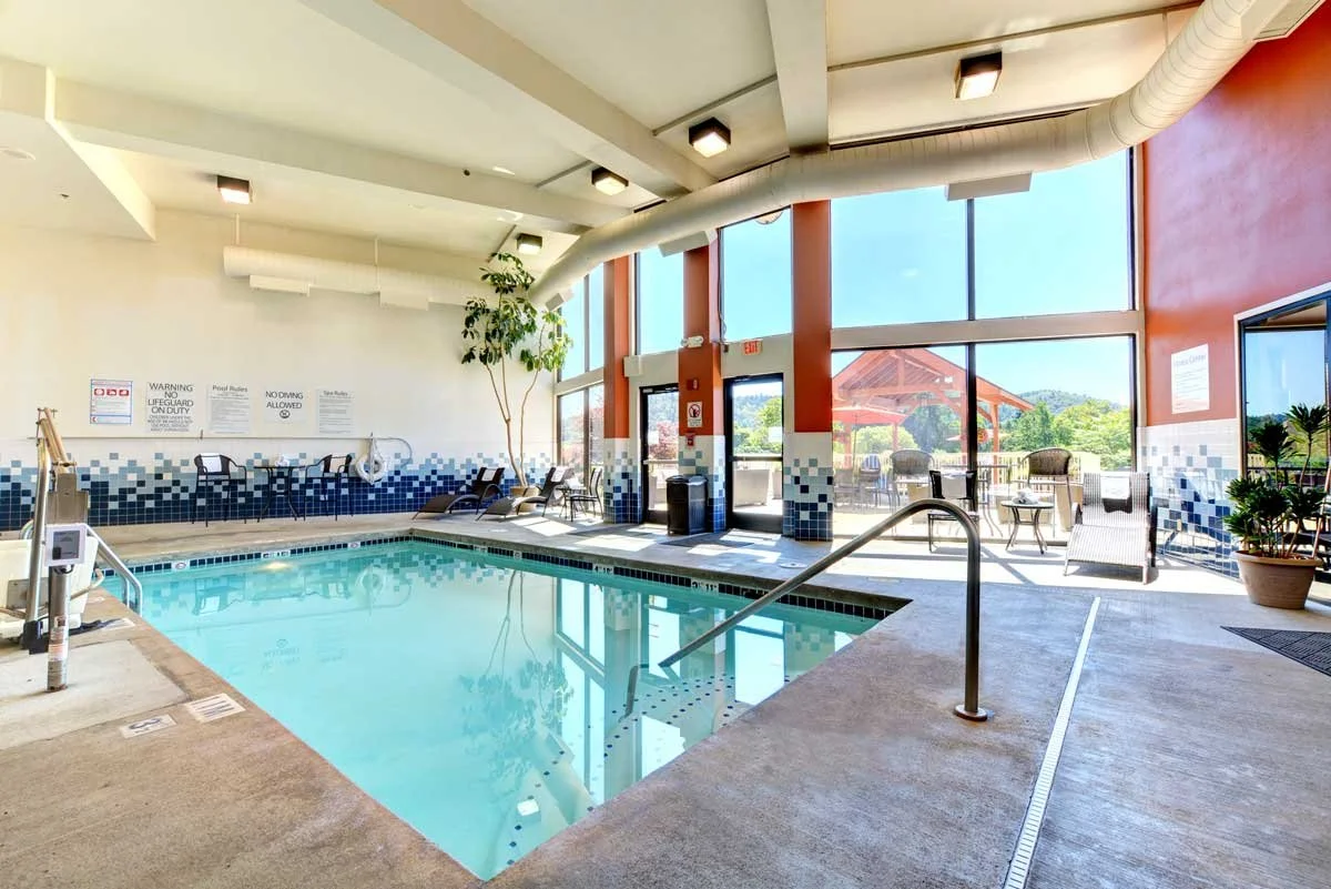 Indoor swimming pool with lounge chairs, large windows and a view of an outdoor pavilion