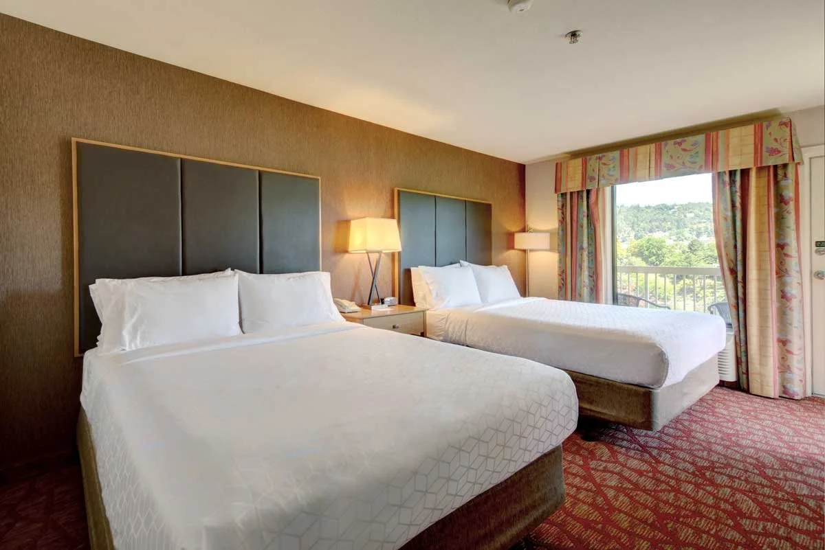 Hotel room with two queen sized beds and nightstand overlooking a private guestroom balcony