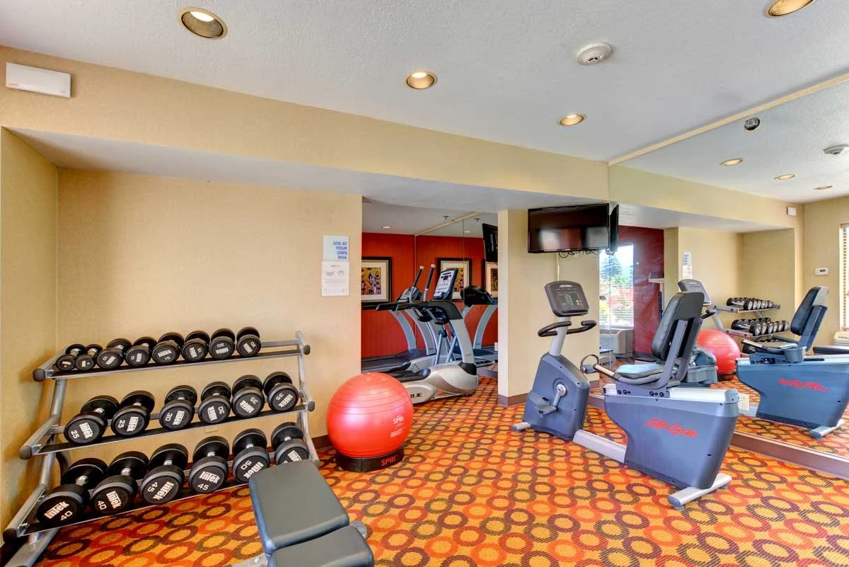Fitness center gym with dumbbells, cardio machines, yoga ball and TV 