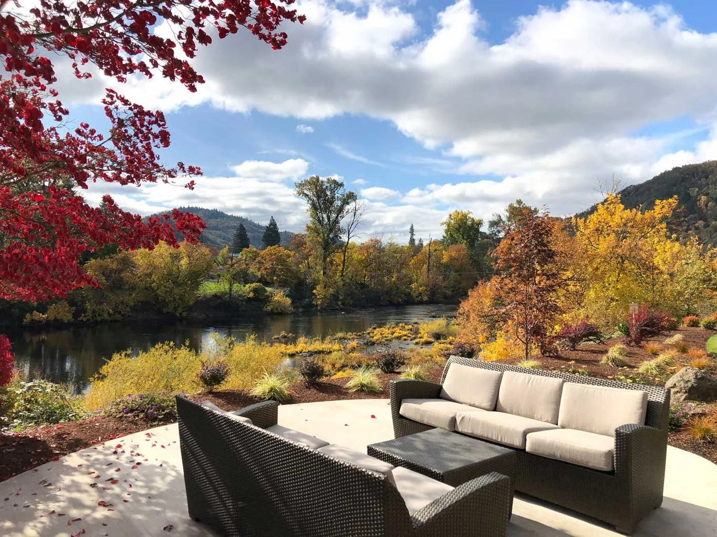 Hotel outdoor patio with lounge sofa seating overlooking a calm river with colorful autumn foliage