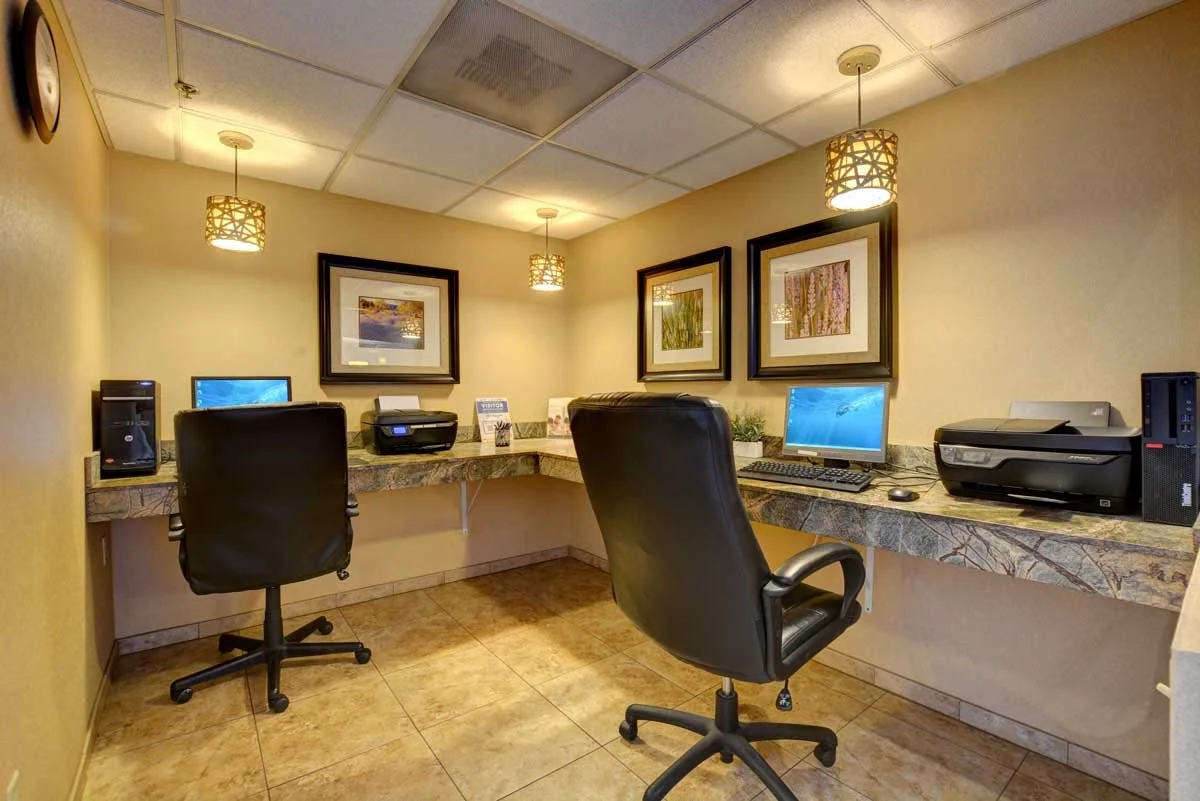 Business center with two computer workstations and two printers in an enclosed room 
