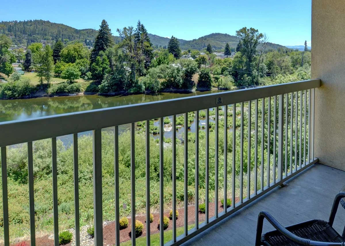 View from guestroom balcony overlooking a river, lush green trees and distant mountains