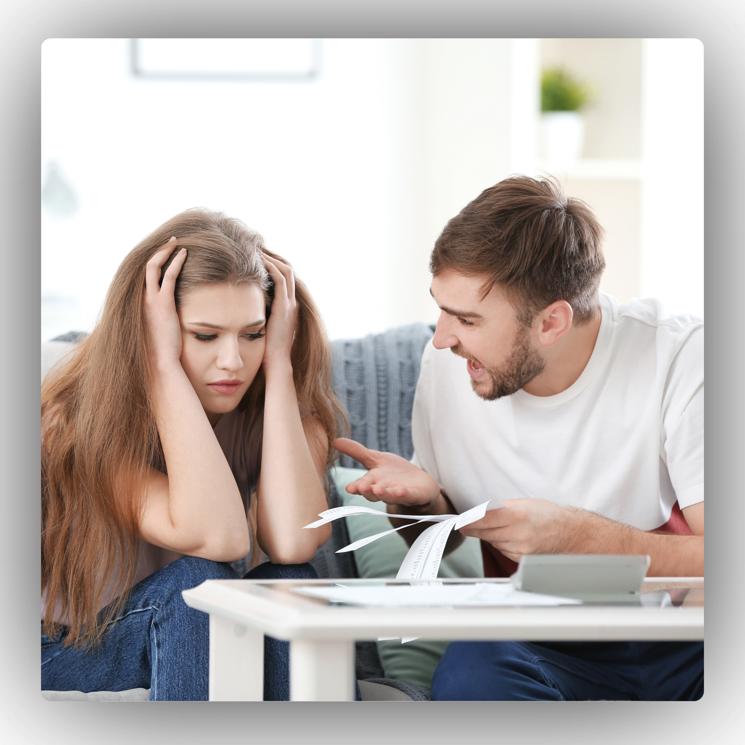 A man shouting at a woman who looks distressed and is holding her head, sitting at a table with papers and a calculator.