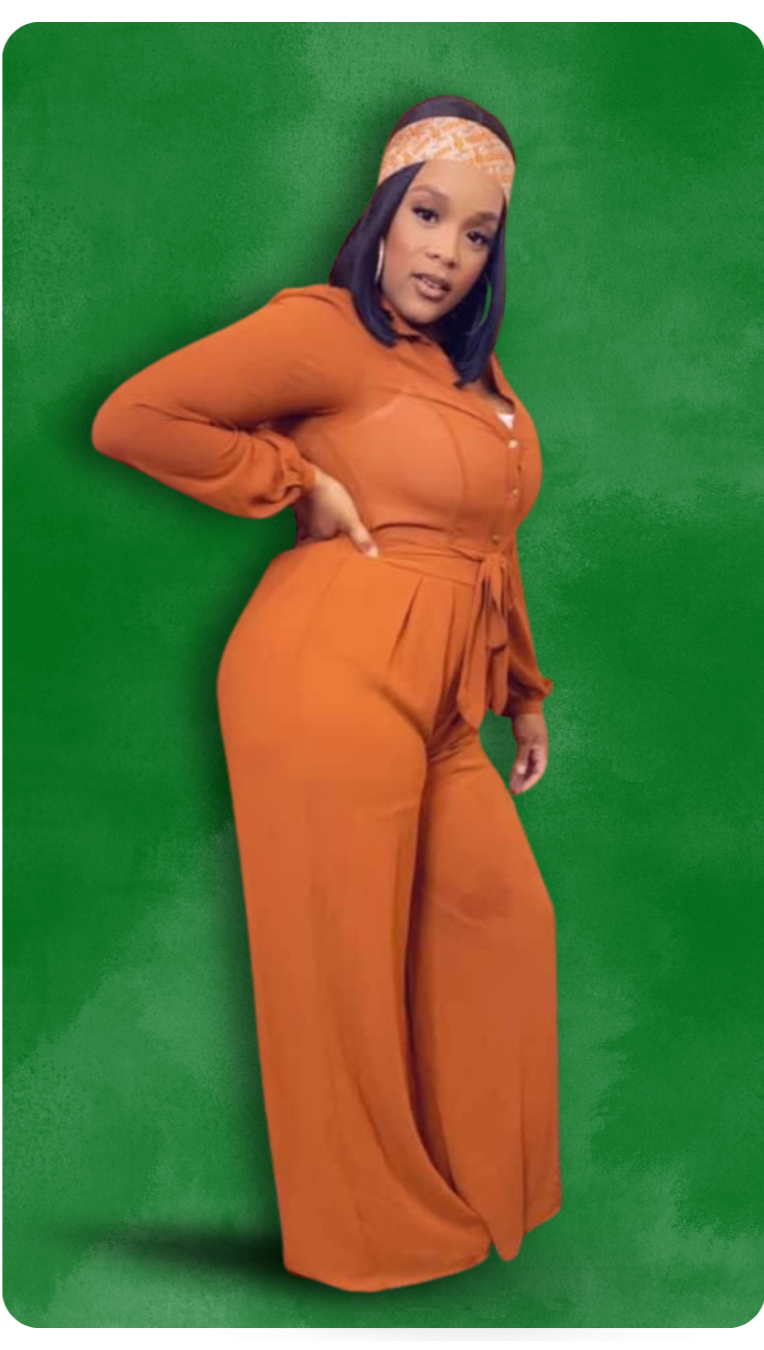 Woman wearing an orange jumpsuit and a patterned headband, standing against a green screen background.