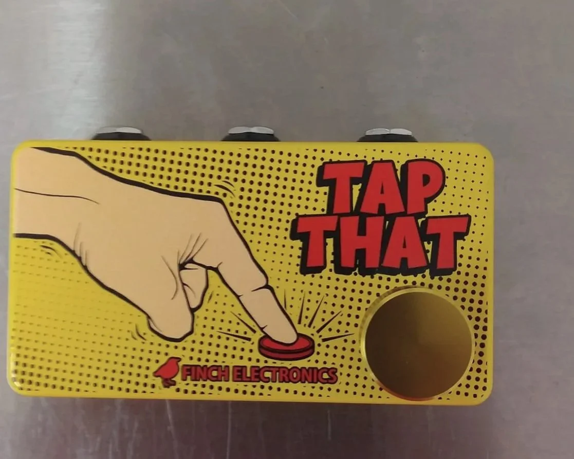 A yellow box with a comic-style illustration of a hand pressing a red button. The box has the words "TAP THAT" in large red letters and "Finch Electronics" written below with a small bird icon.