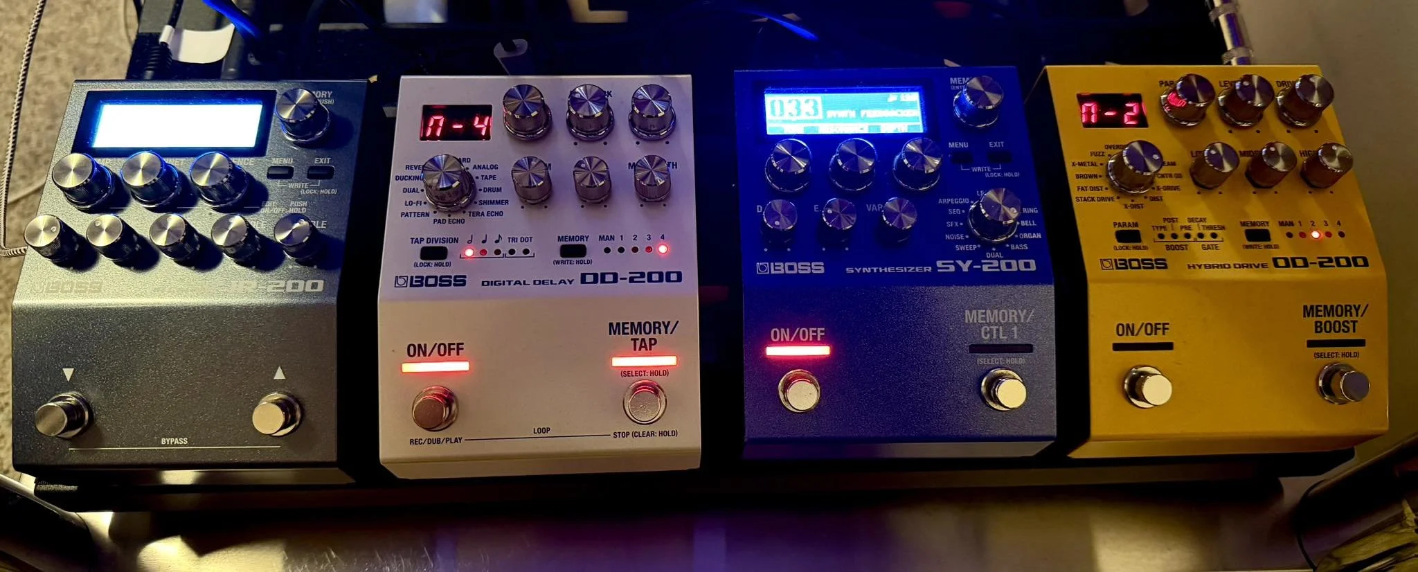 A music synthesizer setup with four effect pedals connected, including Boss DD-200 digital delay, Boss SY-200 synthesizer, Boss DD-200, and Boss DD-200 hybrid drive pedal.