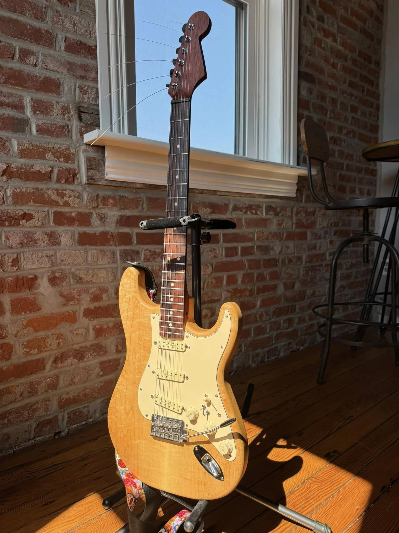 A yellow electric guitar leaning against a brick wall near a window, with sunlight casting a shadow on the wooden floor.