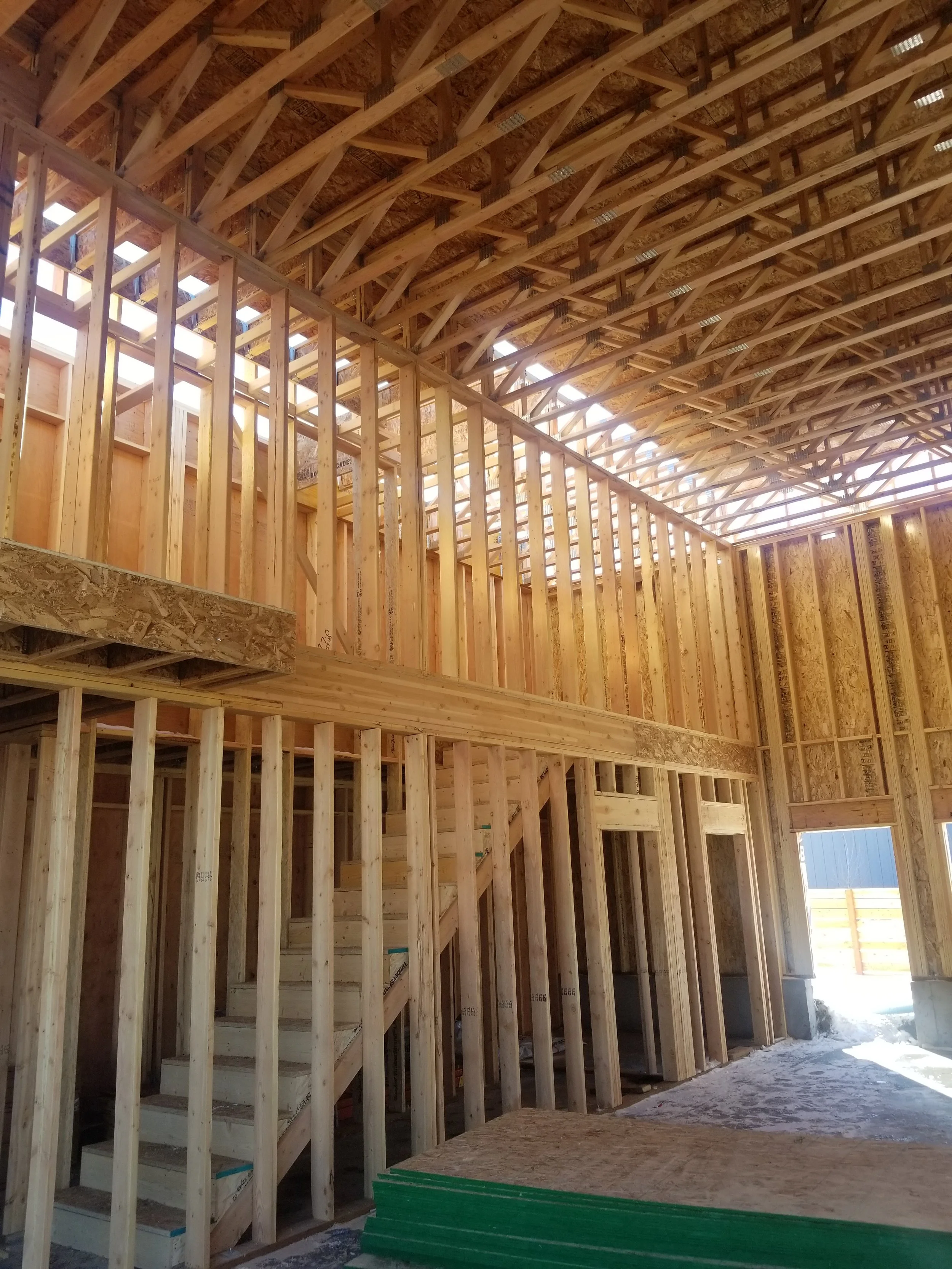 Interior view of a house under construction, showing wooden framing, stairs, and roof trusses.