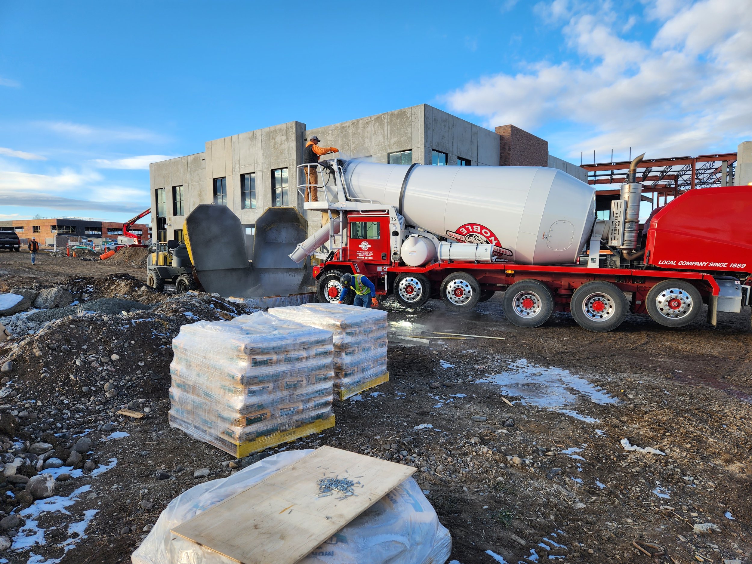 Construction site with a concrete mixer truck pouring cement, construction workers, and building framework in the background.