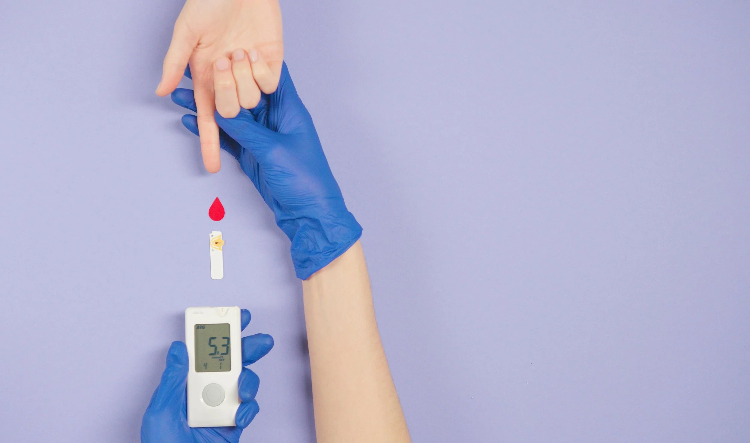Person wearing blue gloves uses a blood glucose meter to test blood from their finger, with a drop of blood and a test strip visible on a lavender background.