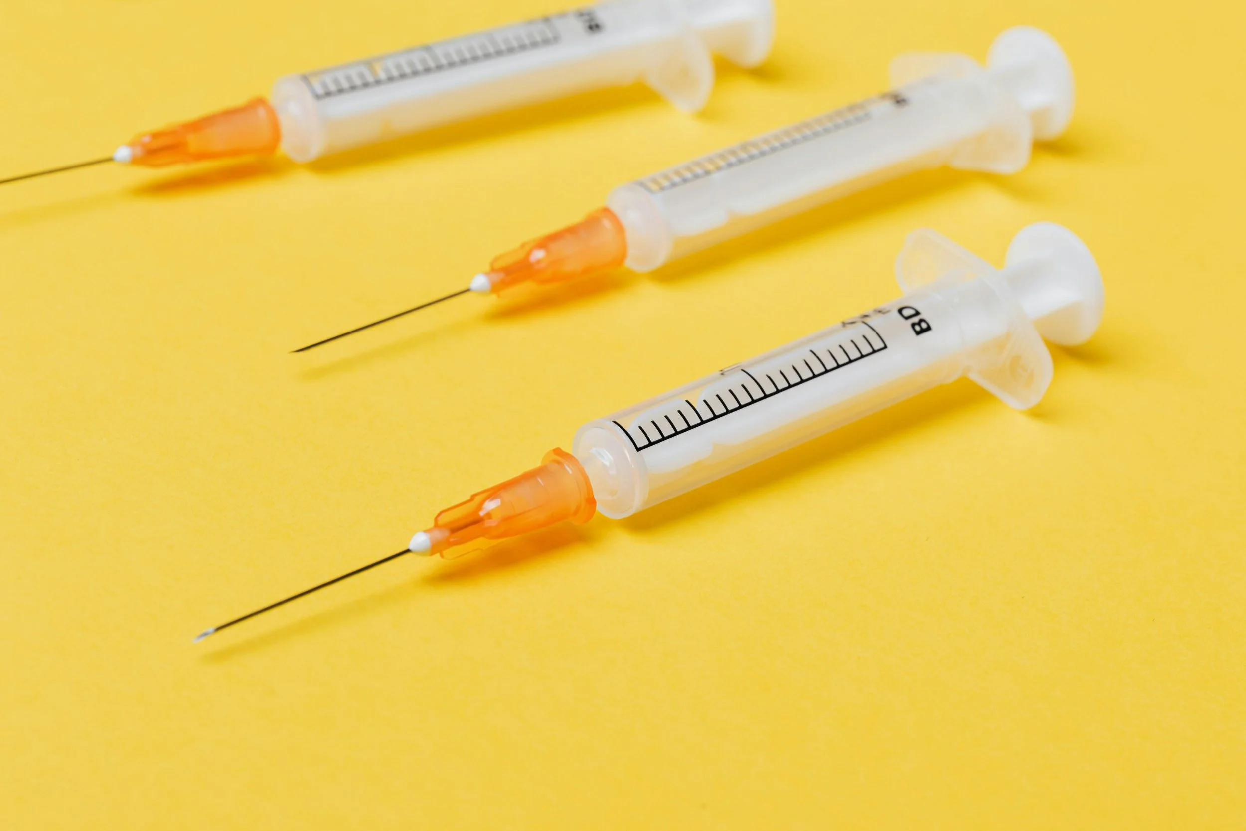 Three syringes with orange needle caps on a yellow background.