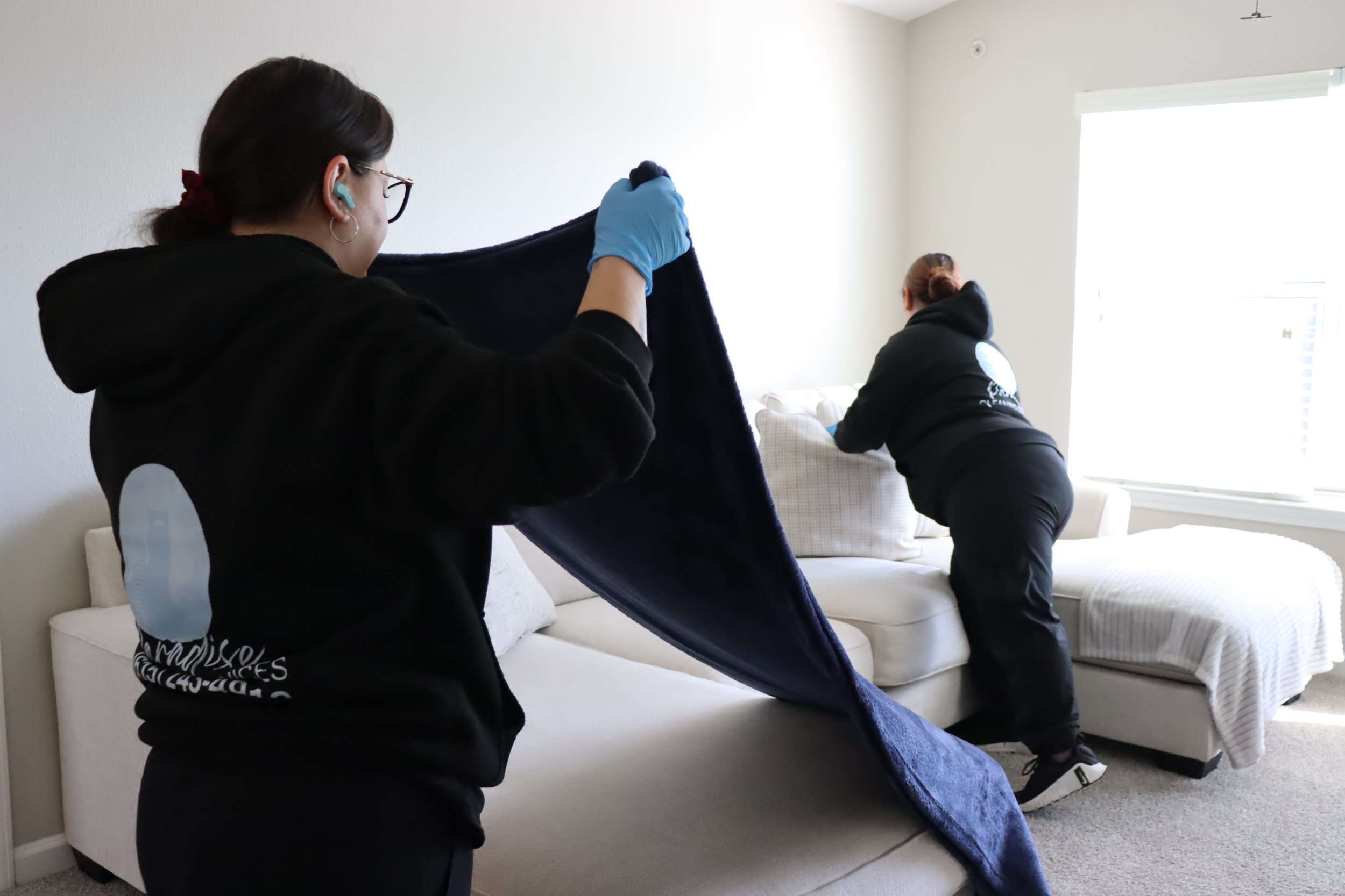 Professional cleaners refreshing living room sofa and folding blankets during home cleaning.