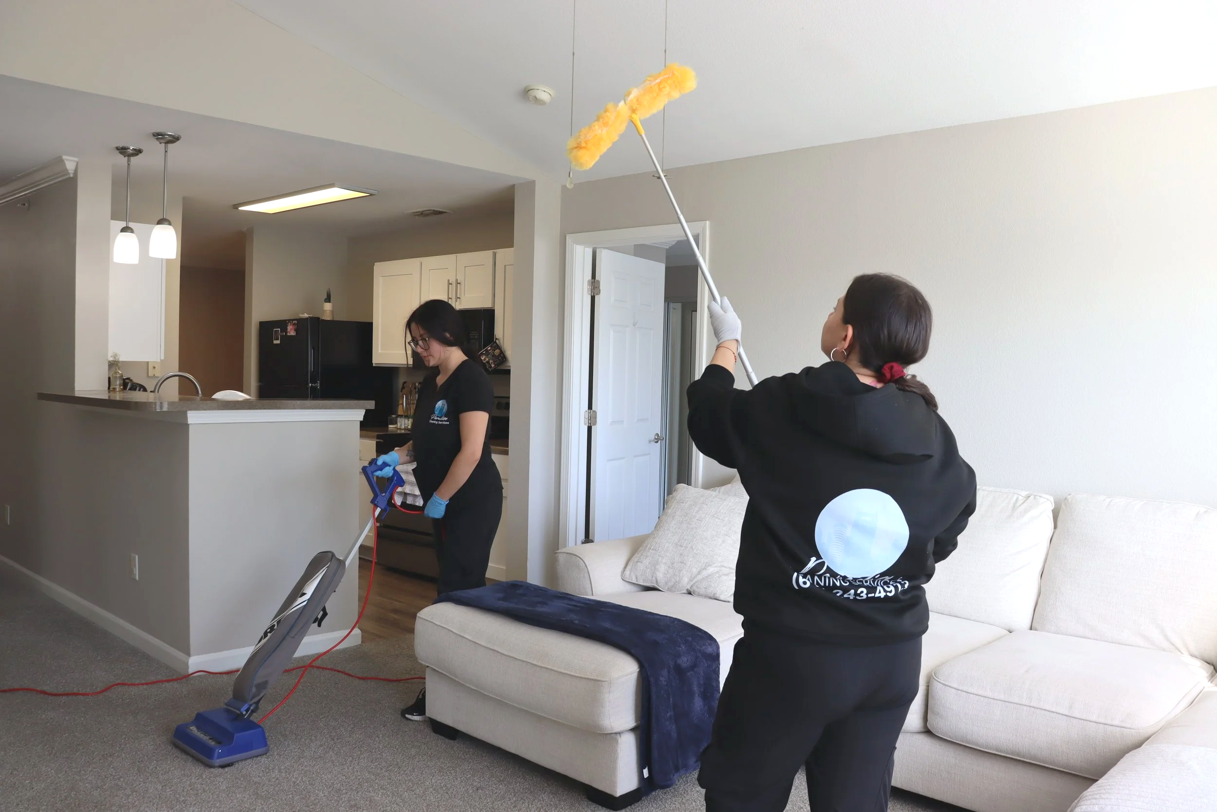 Cleaning team vacuuming floors and dusting high surfaces in residential property.