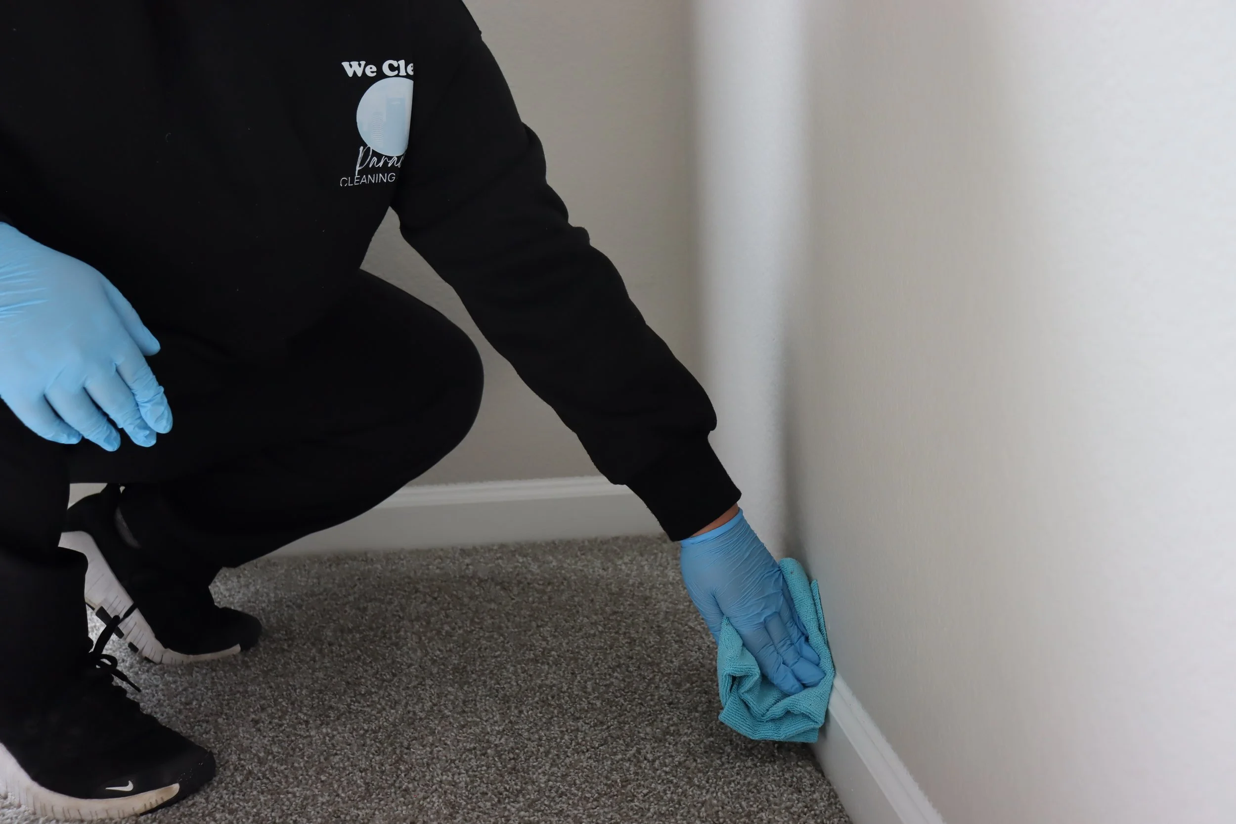 Cleaning professional wiping baseboards and wall corners as part of detailed home cleaning.