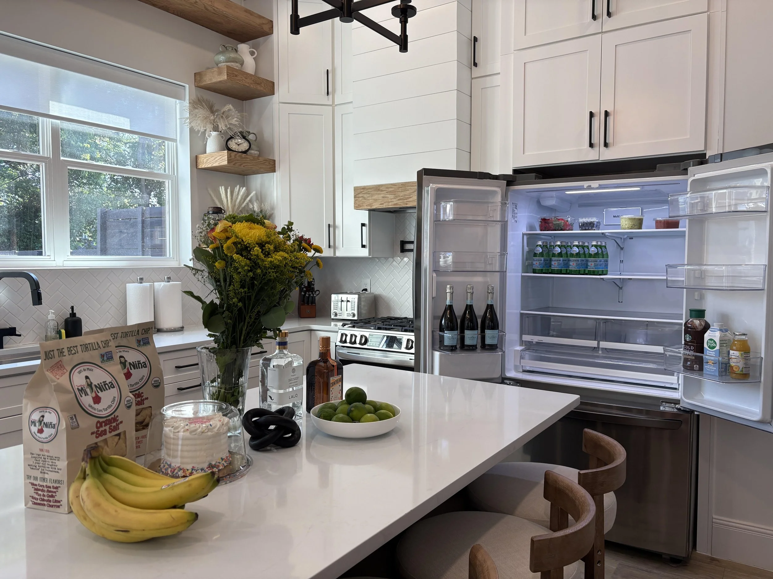 Nashville kitchen stocked with fresh flowers, a cake, fruit, and cocktail ingredients on the island, plus an open fridge stocked with champagne and sparkling water