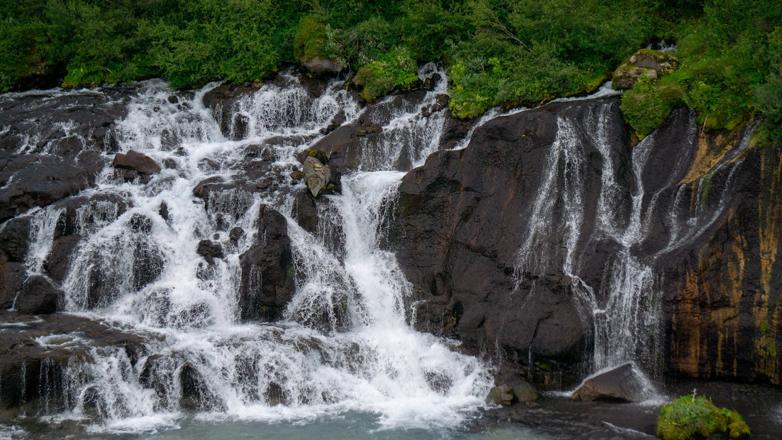 A waterfall cascading over dark rocks with green foliage at the top.