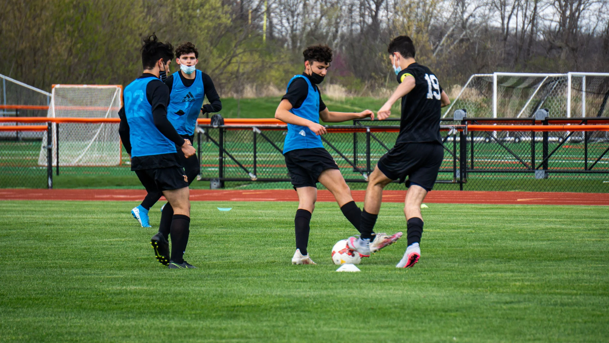 Young soccer players practicing on a grassy field, wearing face masks and soccer uniforms, engaging with a soccer ball during a training session.