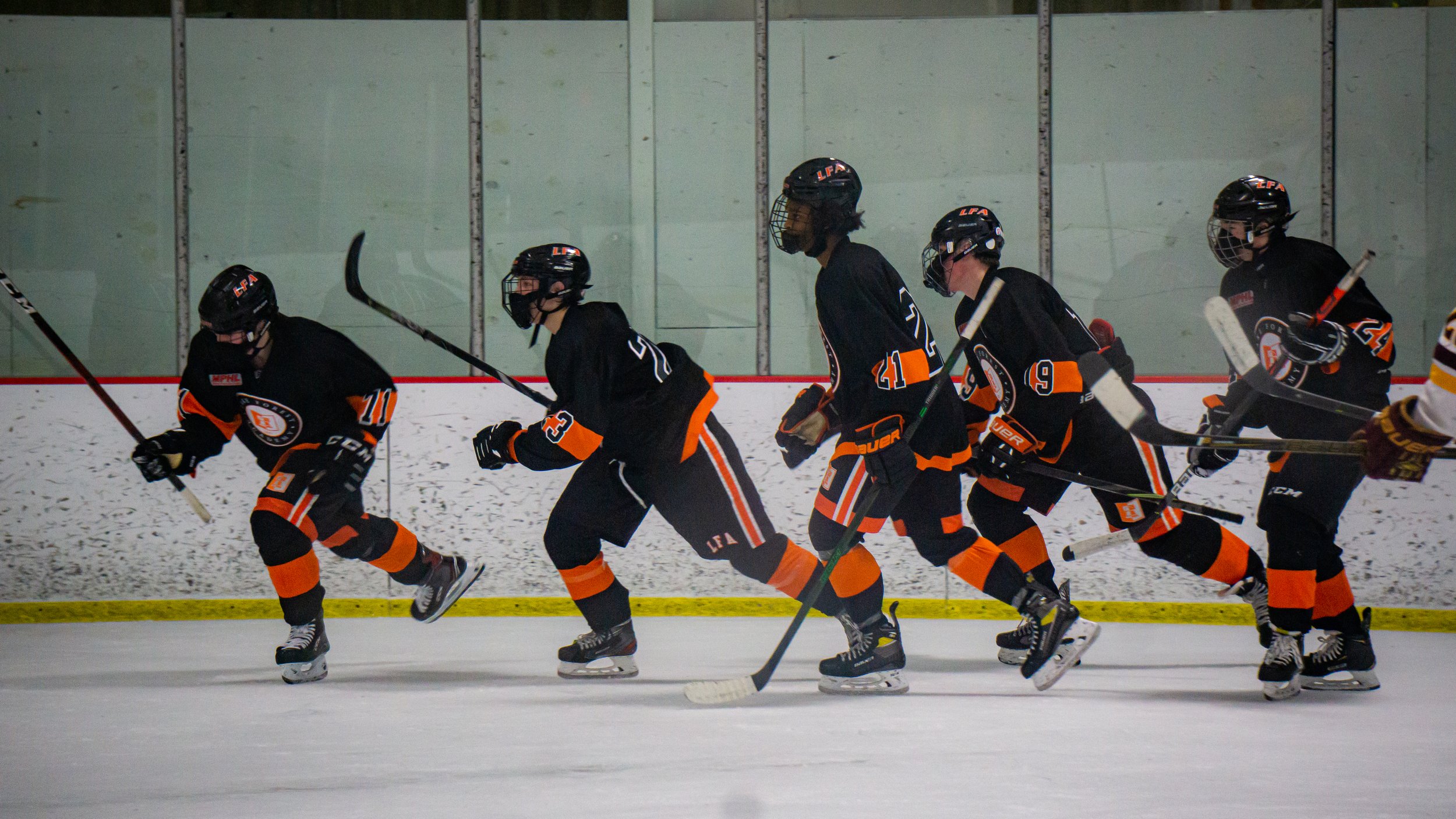 A group of boys in black and orange hockey uniforms skating on an ice rink.