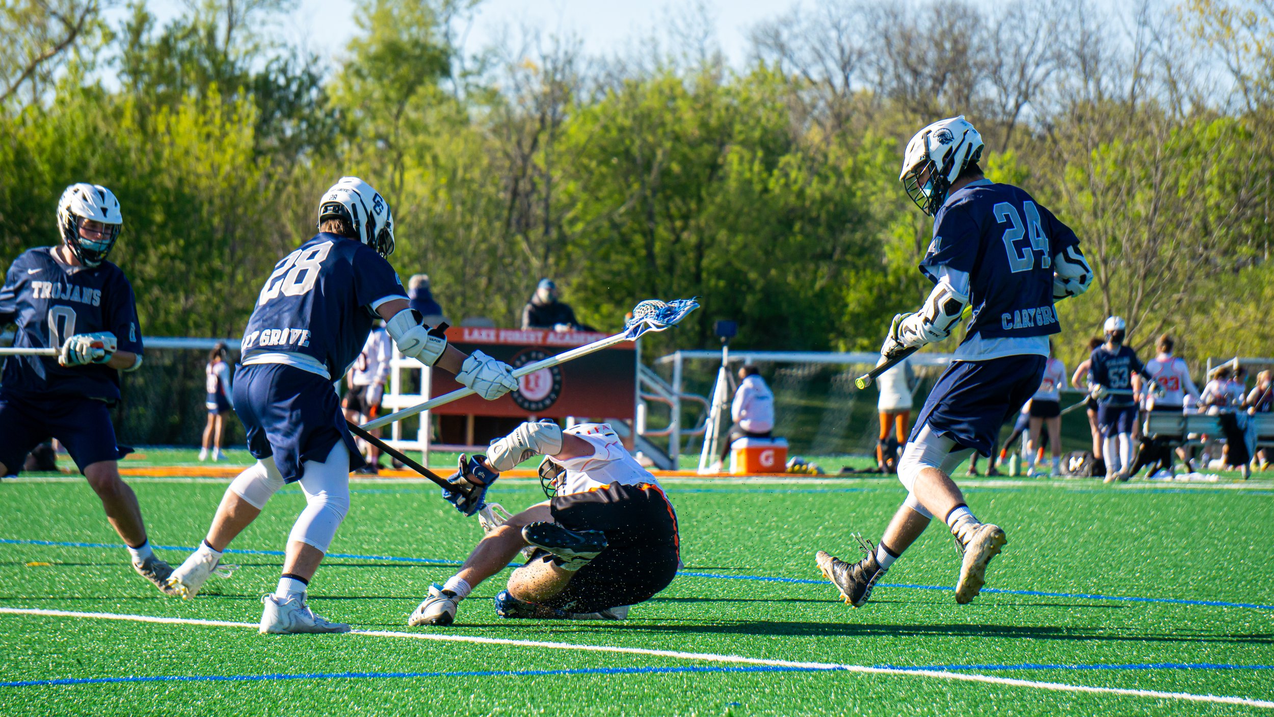 Lacrosse players in blue and white uniforms playing the game on a green turf field during daytime.
