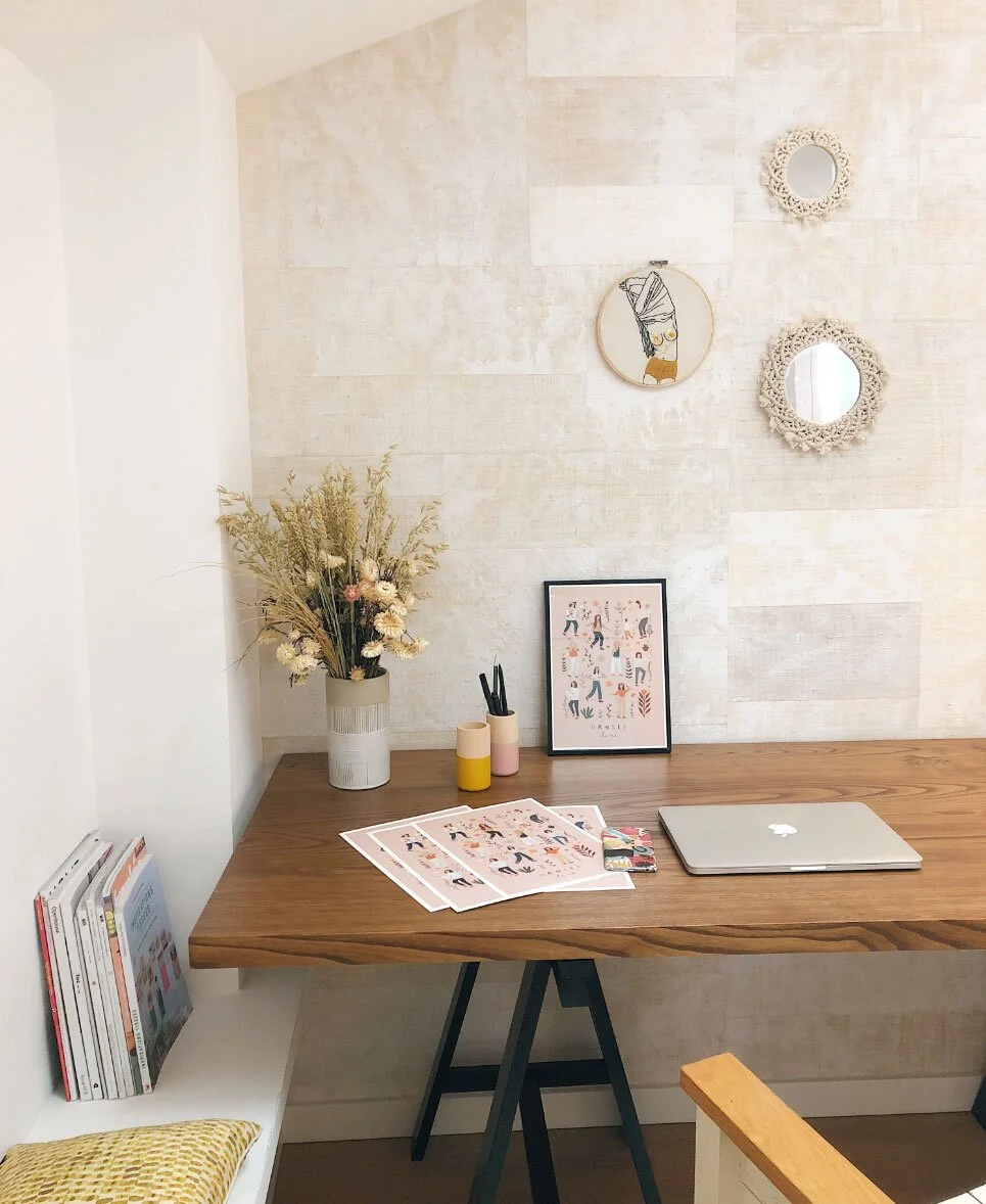 Minimalist home office with wooden desk, laptop, framed art, vases with pens, decorative wall mirrors, and dried flowers in a vase