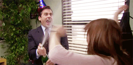 Two people in an office celebrating, one wearing a party hat and holding a noisemaker, the other reaching toward the first person