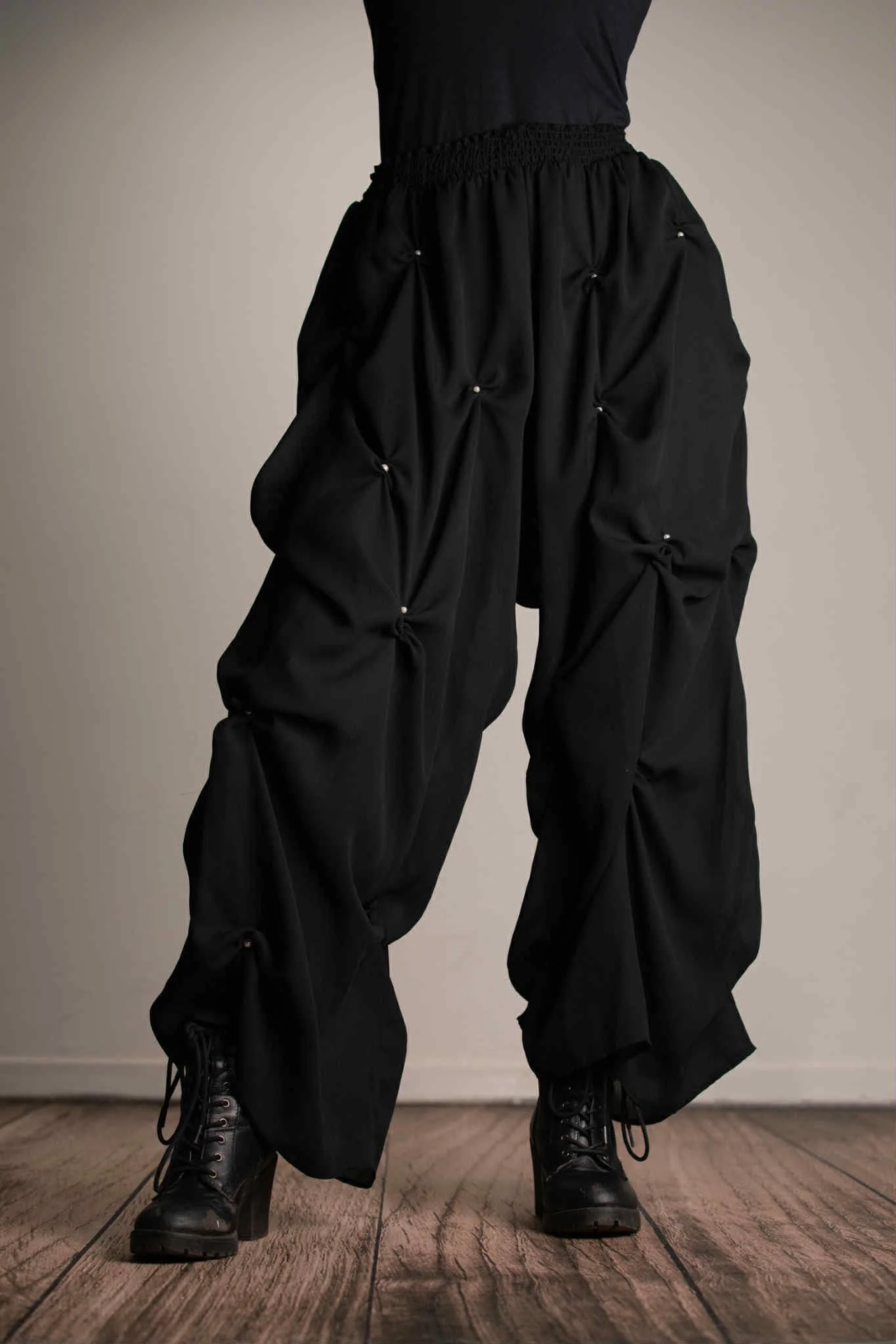 Person wearing black baggy pants with gathered knots and black lace-up boots indoors.