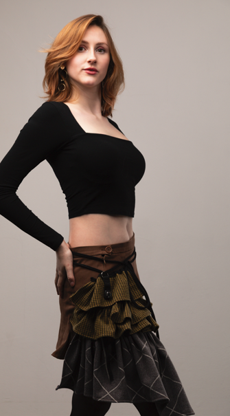A woman with red hair wearing a black long-sleeve crop top and layered skirt.