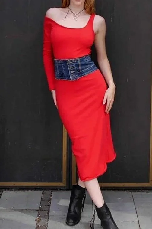 A woman wearing a red off-the-shoulder dress with long sleeves, a denim waist belt, and black ankle boots standing against a black background.