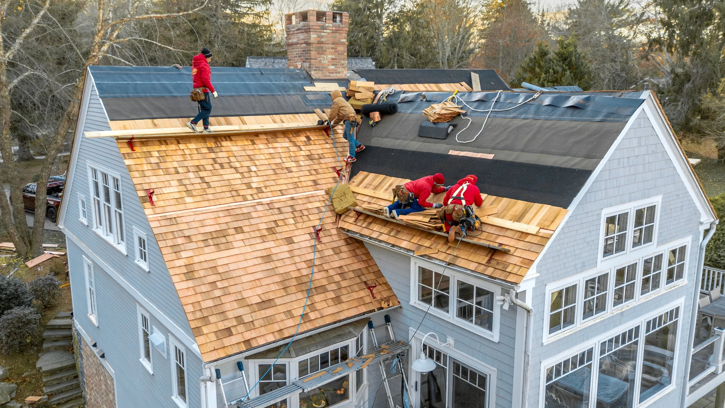 Workers installing new roofing shingles on a multi-story house.