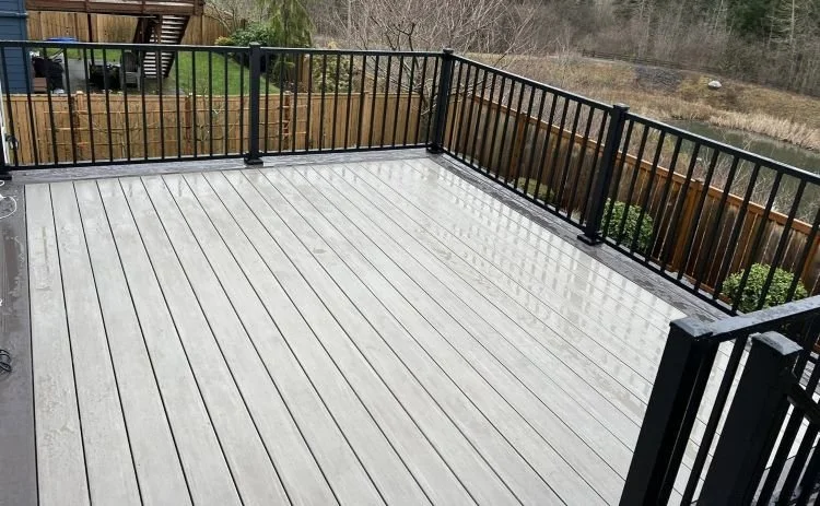 Elevated composite deck with black aluminum railings overlooking a wooded backyard in Snoqualmie, WA, designed for sloped terrain and long-term durability.