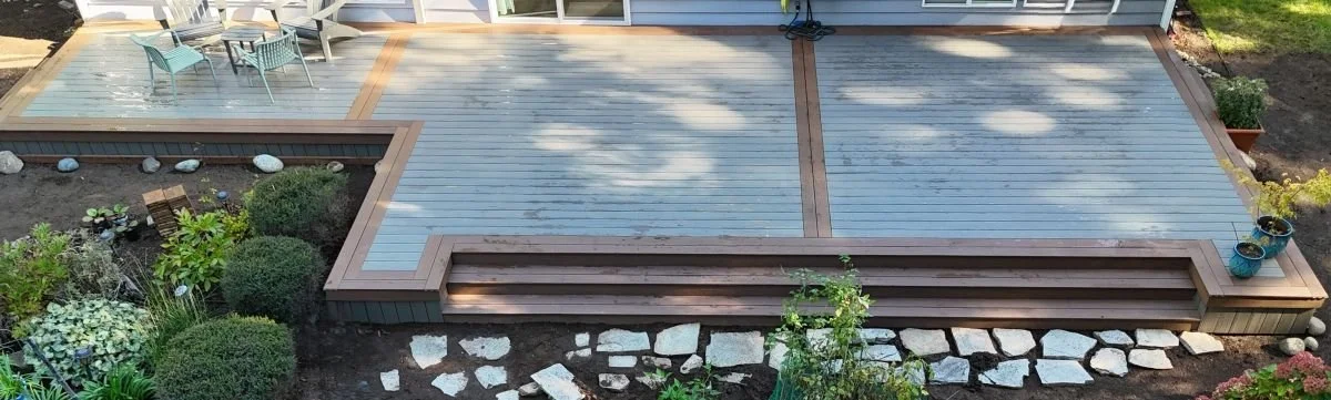 Composite deck replacement in Sammamish WA with two-tone decking, Silver Maple boards, Brown Oak trim, and wide built-in stairs across backyard patio