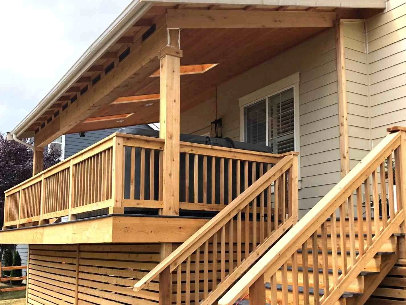Covered deck with permanent roof structure integrated into existing home framing and stair system