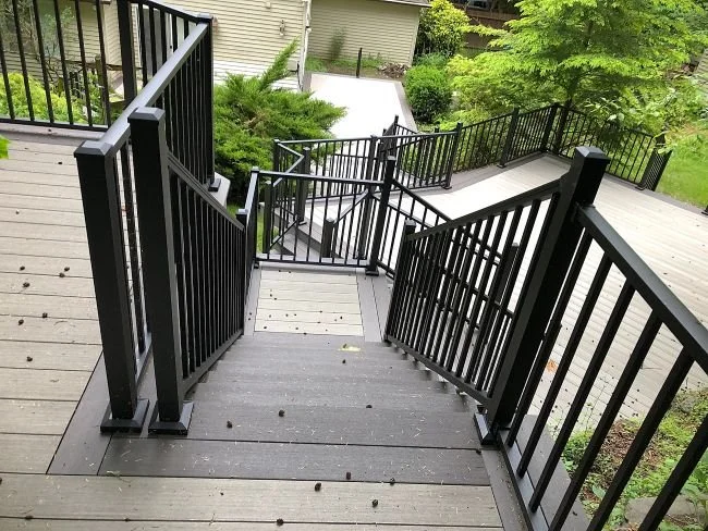 Multi-level deck construction featuring composite decking, multiple stairways, and black aluminum railings designed for a sloped backyard by Petra Decks in King County, WA.