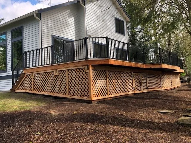 Elevated deck in Renton, WA featuring black aluminum railings, cedar lattice skirting, and a built-in staircase, built by Petra Decks.