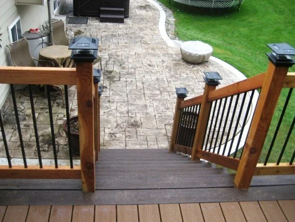 Deck stairs with composite decking, wood rail posts, metal balusters, and post cap lights showing typical maintenance areas