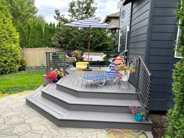 Completed composite deck construction in Maple Valley WA backyard with multi-level steps, railing, and outdoor seating area designed for everyday use