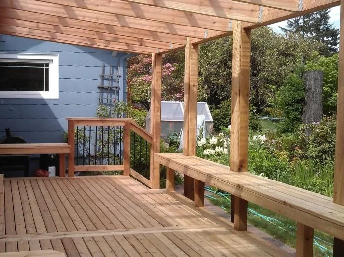 Partially covered deck with pergola-style roof and built-in bench, showing open-air overhead structure and wood framing