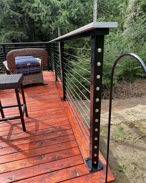 Custom deck railing installation featuring black aluminum posts, stainless steel cable railing, and wood top rail completed by Petra Decks in King County, WA.