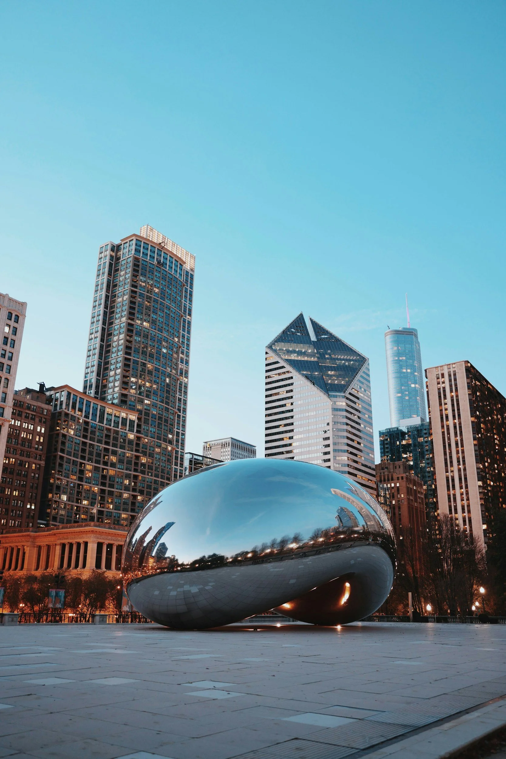 City skyline with tall buildings and a shiny, reflective sculpture in the foreground.