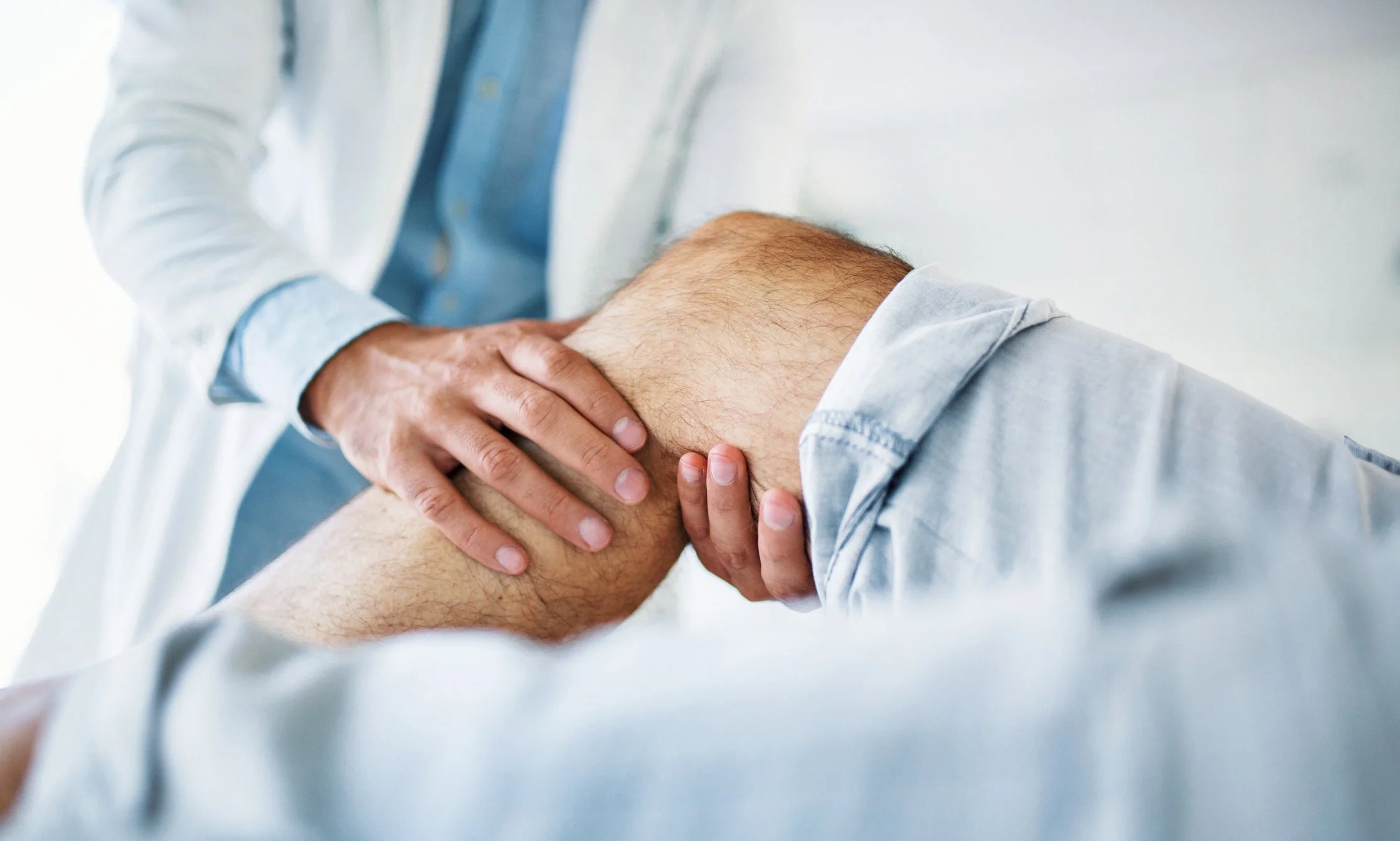 Medical professional examining a patient's knee, holding it gently during a consultation.
