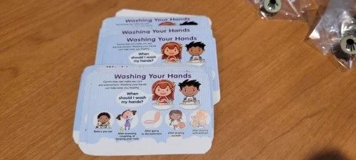 Instruction sheets on handwashing with illustrations, placed on a wooden table.