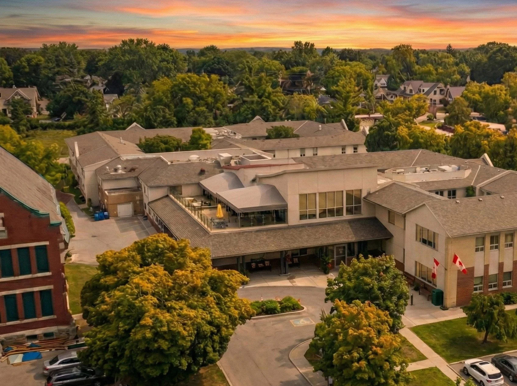 Aerial view of a large multi-story building with flagged entrance, surrounded by trees and a parking lot during sunset.